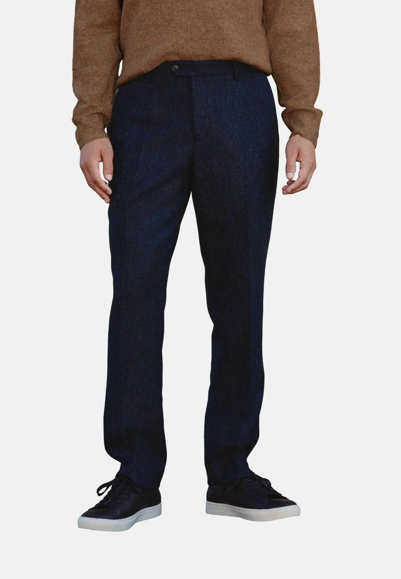 Marineblauwe wollen broek met een rechte pasvorm, voorzien van een platte voorkant, riemlussen en zijzakken, gecombineerd met zwarte schoenen en een bruine trui.