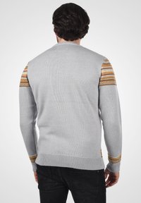 Grauer gestrickter Pullover mit gemusterten goldenen und orangefarbenen Streifen an den Schultern. Verfügt über einen gerippten Kragen und Ärmelbündchen. Strukturiertes Material.