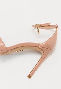 Rosa lakkert skinnhæl sandaler med ankelrem, detalj av gullspenne, og spiss tå, som fremhever en glatt tekstur og strømlinjeformet design.