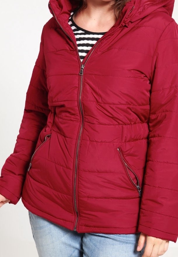 Red puffer jacket with a hood, featuring a zip closure, two front pockets, and quilted texture. Worn over a black and white striped top.