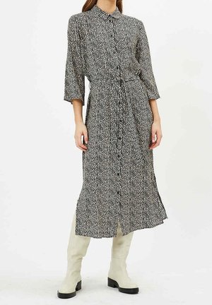 Vestido de patrón en blanco y negro con cuello, mangas largas, botones en el frente y un lazo en la cintura, combinado con botas crema hasta la rodilla.