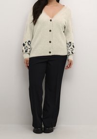 Ljusgrå stickad kofta med V-ringning, med svart blommig brodyr på ärmarna, sju knappar och ribbade ärmslut, kombinerad med svarta byxor.