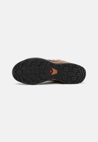 Trail running shoe outsole featuring a rugged black rubber tread pattern with raised lugs for grip, accented by a red triangular detail.