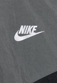 Sivi tekstil s istaknutim bijelim Nike logotipom. Materijal ima nabranu teksturu s glatkom završnom obradom i jednostavnim dizajnom.