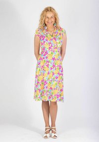 Blommig klänning med ett livligt flerfärgat mönster av trianglar och ananaser. Korta ärmar, figursydd midja, knälång, kombinerad med vita sandaler.