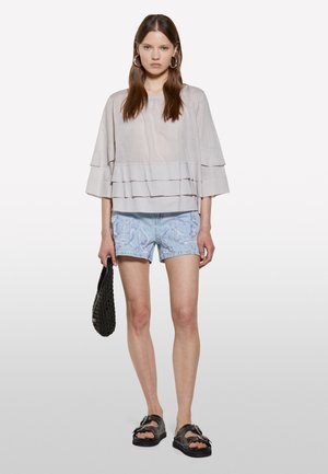 Light gray, layered top with wide sleeves, paired with light blue embroidered denim shorts. Black woven bag and chunky black sandals complete the look.