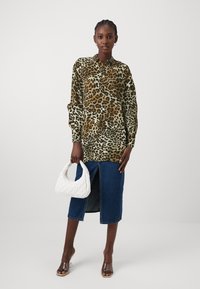 Blusa a maniche lunghe con stampa leopardata e bottoni; abbinata a una gonna di jeans con spacco frontale. La modella tiene una borsa a tracolla bianca trapuntata.