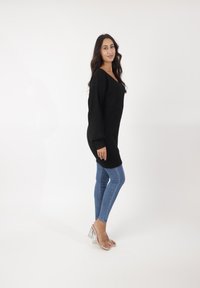 Pull en maille noir oversize à manches longues, associé à un jean skinny bleu et des sandales à talons blocs transparents. Design simple et texturé.