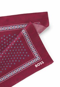 Burgundy patterned scarf with blue and white geometric designs along the edges, featuring a printed logo in white on one corner.