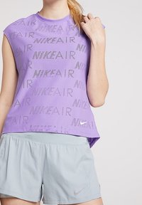 Top sin mangas morado con un patrón de texto perforado "NIKE AIR" y escote redondeado, combinado con pantalones cortos gris claro que presentan bolsillos laterales.