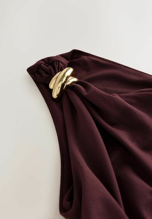 Burgundské látkové tričko s uzlovým designem na rameni, s hladkým, lesklým zlatým kulatým akcentem. Měkká textura a hladké linie.