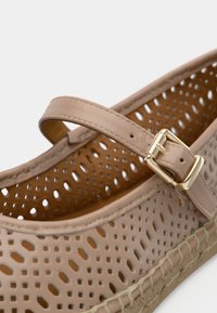 Μπεζ δερμάτινο παπούτσι με διάτρητα σχέδια και λουράκι με αγκράφα, με σόλα από πλεγμένο ζεϊμπέκικο. Το εσωτερικό είναι λείο και σε αποχρώσεις ταμπά, προσφέροντας άνετη εφαρμογή.