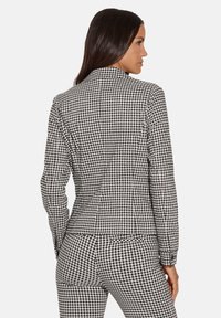 Zwart-wit geruite blazer met een gestructureerde silhouet, aansluitende pasvorm en lange mouwen. Glad stof met een kraag en naden.