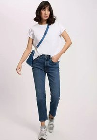 Biała krótki rękaw t-shirt, niebieskie dżinsy z wysokim stanem oraz szare sneakersy. Modelka trzyma małą niebieską torebkę na krzyż. Codzienny strój.