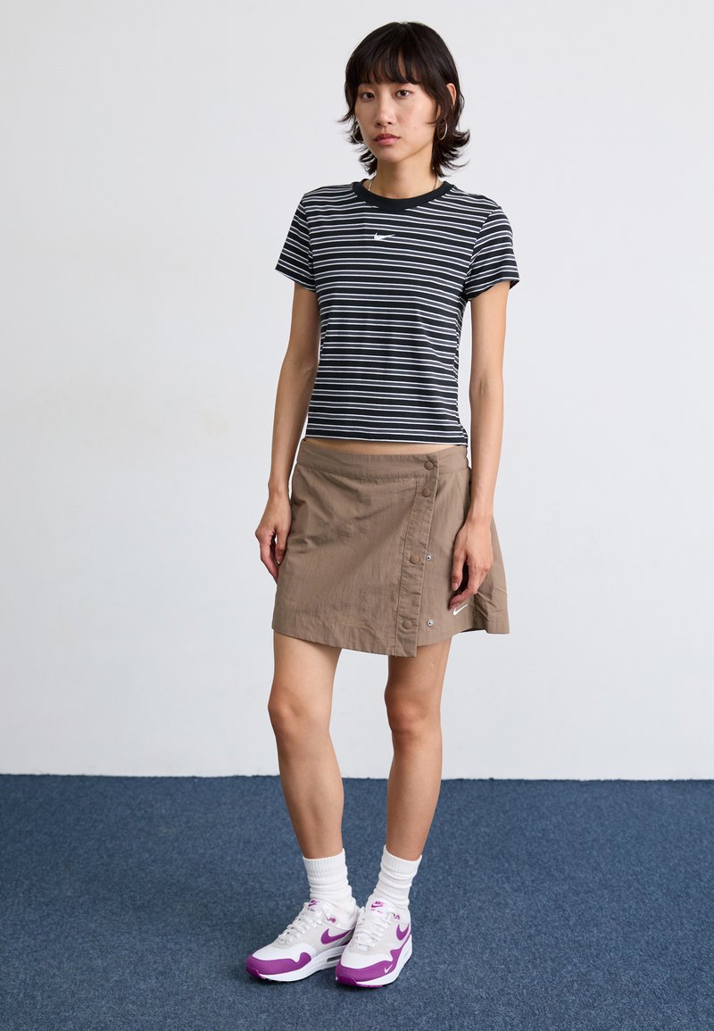 Zwart-wit gestreepte korte mouw top met een ronde hals, gecombineerd met een tan kleurige rok met knopen aan de voorkant en witte sneakers met paarse accenten.