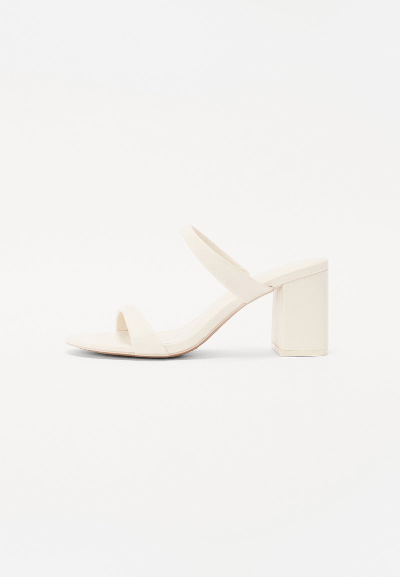 Sandalia de tacón bloque beige con dos tiras anchas en la parte superior, superficie lisa y diseño de punta abierta.