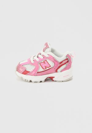 Chaussure de sport enfant en blanc et rose avec lacets, tissu en mesh et logo de la marque sur le côté visible sur fond uni.