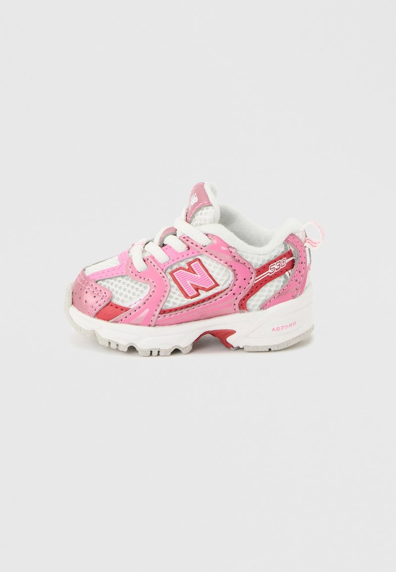 Chaussure de sport enfant en blanc et rose avec lacets, tissu en mesh et logo de la marque sur le côté visible sur fond uni.