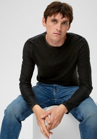 Zwart T-shirt met lange mouwen en ronde hals, gecombineerd met blauwe denim jeans. De stof heeft een lichte textuur en de pasvorm is casual.