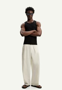 Black tank top, cream wide-leg pants, and flip-flops. Accessories include sunglasses and a silver chain. Smooth, relaxed fabric texture.