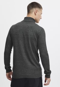 Dunkelgrauer Strickpullover mit hohem Kragen, langen Ärmeln sowie gerippten Bündchen und Saum; glatte Textur mit tailliertem Schnitt.