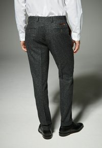 Pantalones de lana gris texturizados con un diseño ajustado, dos bolsillos traseros y trabillas para cinturón, combinados con zapatos de cuero negros.