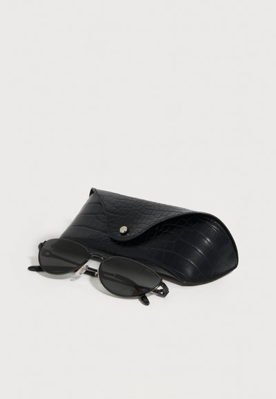 Μαύρα οβάλ γυαλιά ηλίου με μεταλλικά πλαίσια τοποθετημένα δίπλα σε μαύρο υφασμάτινο δερμάτινο θήκη με κλείσιμο με κουμπί σε λευκό φόντο.