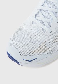 Αθλητικό παπούτσι ανοιχτού γαλάζιου χρώματος με πλεκτό επάνω μέρος από διχτυωτό υλικό, υφή με λεπτομέρειες και αντίθετη σόλα σε σκούρο μπλε με κίτρινες λεπτομέρειες.