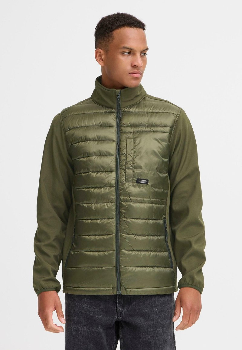 Jachetă verde căptușită cu guler în picioare, având un fermoar frontal și o buzunar pe piept. Materialul este nylon cu o textură netedă.
