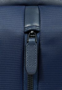 Marineblauw gestructureerd stof met een glad leren ritssluitingtrekker, voorzien van een donker metalen rits en versterkte stiksels langs de randen.