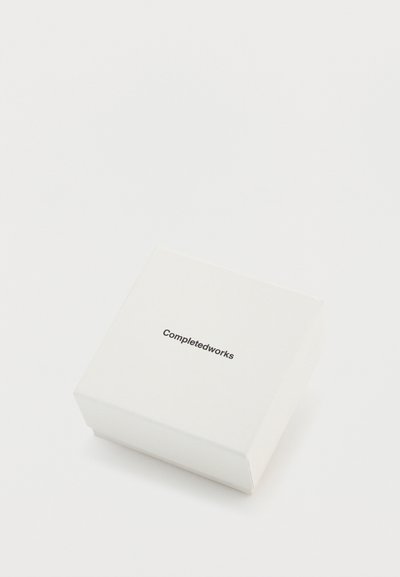 Cutie pătrată albă cu finisaj mat, cu textul imprimat „Completedworks” în negru pe suprafața superioară.