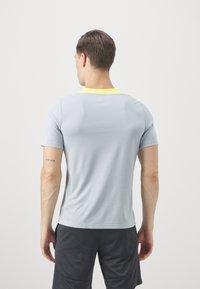 Light grey athletic t-shirt with short sleeves, textured fabric, a slim fit, and a bright yellow collar. Worn with dark shorts.