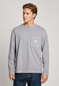 Long-sleeve gray cotton T-shirt with a chest pocket and a label, set against a neutral background. Soft texture, relaxed fit.