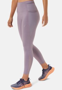 Helle lila hochgeschnittene Leggings mit glatter Textur und Seitentasche; kombiniert mit dunkelblauen Sportschuhen mit orangenen Sohlen.