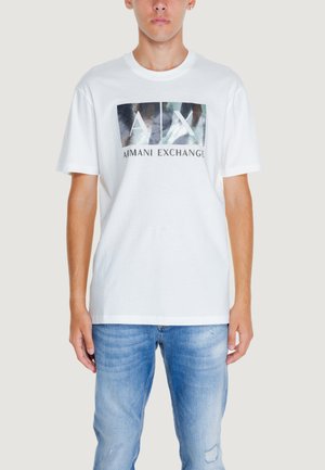 T-shirt bianco in cotone con un design grafico che presenta il testo 'AX' e 'Armani Exchange', abbinato a jeans in denim blu.