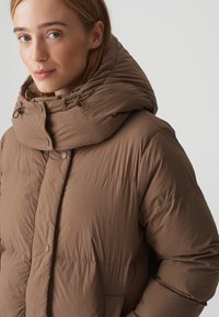 Braune gepolsterte Jacke mit hohem Kragen und verstellbarem Kapuze. Leichtes, strukturiertes Material mit Knopfverschluss vorne und sichtbaren Nähten.