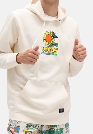 Osoba nosząca kremową bluzę z kapturem Vans z grafiką słonecznika i motyla oraz napisem „Vans for the Earth”. Bluza ma przednią kieszeń i sznurki.