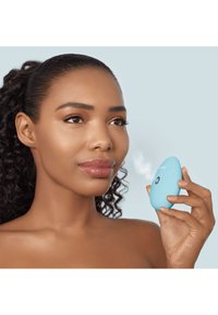 Un dispositif facial bleu en forme d'œuf tenu dans une main, avec un bouton et une fonction de brume. Texture lisse sur un fond clair.