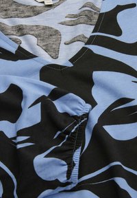 Kurzärmliges T-Shirt in Hellblau mit einem schwarzen und grauen abstrakten Muster. Der Stoff besteht aus weicher Baumwolle und hat ein V-Ausschnitt-Design mit kontrastierenden Nähten.