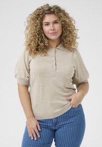 Beige polo met korte mouwen, een kraag en een vijfknops sluiting. Zachte textuur, fitted model, geribbelde manchetten en een gladde afwerking.