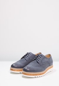Scarpe in pelle grigia con dettagli perforati, punta rotonda e chiusura con lacci. Presentano una suola in beige e bianco a contrasto con accentuazioni testurizzate.