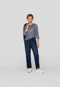 Langärmliges Oberteil mit navyblauen und weißen Streifen, kombiniert mit hoch geschnittenen, dunklen Jeans. Weiße Turnschuhe vervollständigen das Outfit.