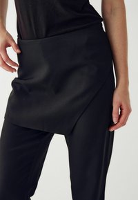 Melnas bikses ar apģērbu dizainu un gludu tekstūru. Iekļauj platāku jostasvietu un sānu kabatas, nodrošinot elegantu siluetu.