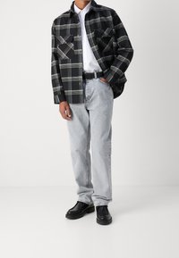 Schwarz-weißer Karobluse mit zwei Brusttaschen, kombiniert mit hellen Jeans und schwarzen Schuhen. Die Bluse hat eine lockere Passform und eine durchgehende Knopfleiste.