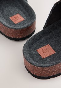 Semelle intérieure en feutre gris avec une semelle extérieure de style liège marron. Un patch carré en cuir affiche le logo de la marque "NEXT". Bout rond avec une base plate.
