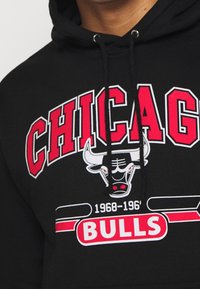 Sudadera negra con la inscripción "CHICAGO" en letras rojas en negrita, "BULLS" en blanco y un gráfico de un toro. Material de algodón con cordón ajustable.