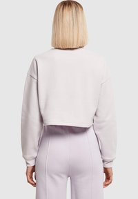 Trumpas švarkelis iš šviesiai pilkos fliso medžiagos su nusvirusiomis pečių linijomis ir ribinėmis rankogaliais, derinamas su šviesiai violetinėmis, aukštu liemeniu kelnėmis.