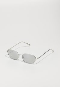 Lunettes de soleil en métal argenté avec des verres gris ovales, des branches fines et un design minimaliste. Les verres présentent une légère qualité réfléchissante.