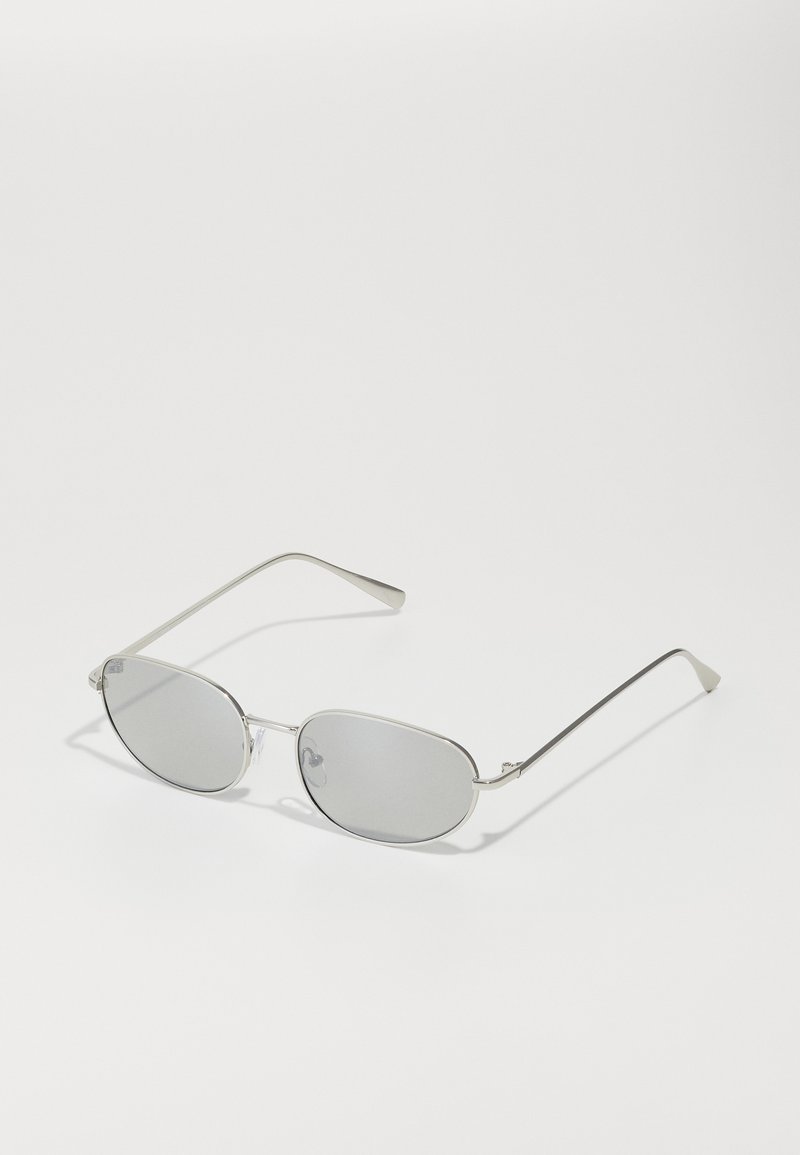 Lunettes de soleil en métal argenté avec des verres gris ovales, des branches fines et un design minimaliste. Les verres présentent une légère qualité réfléchissante.