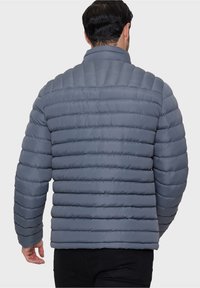 Giubbotto imbottito grigio con design a righe orizzontali, colletto alto e polsini elastici. Texture liscia, leggero e con una finitura leggermente lucida.